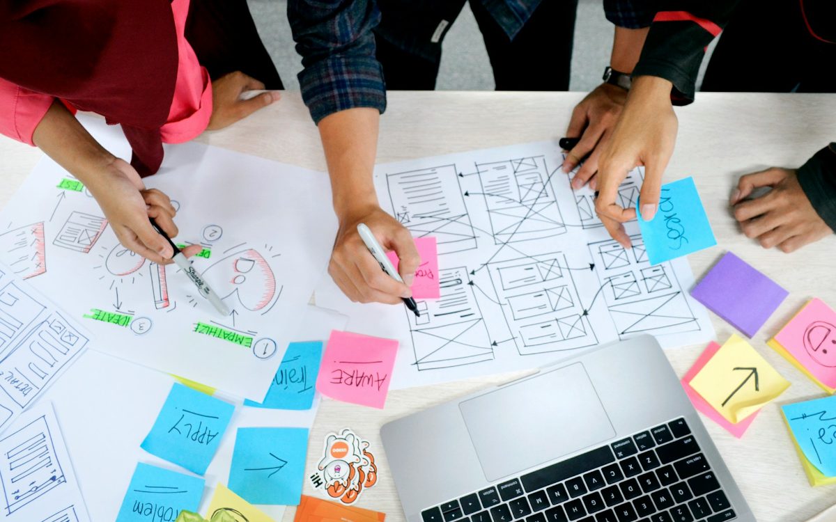A team sketching workflow wireframes and sticky notes around a laptop