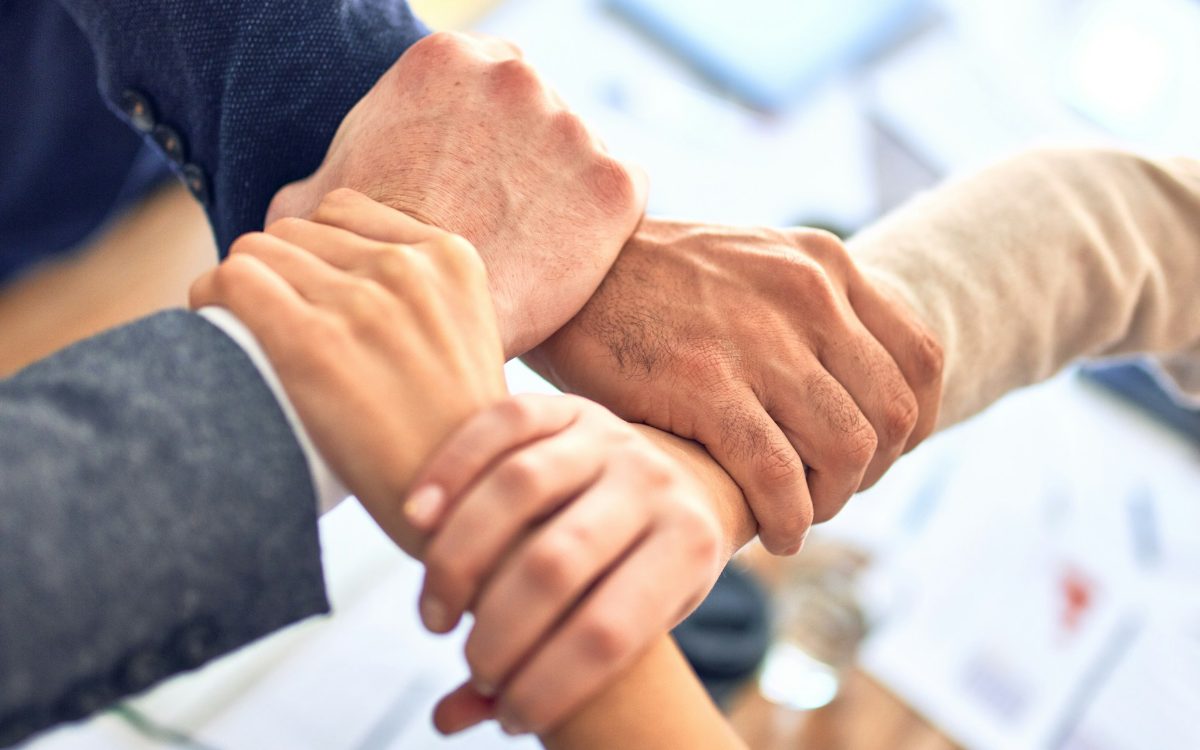 Four colleagues linking hands over a meeting table